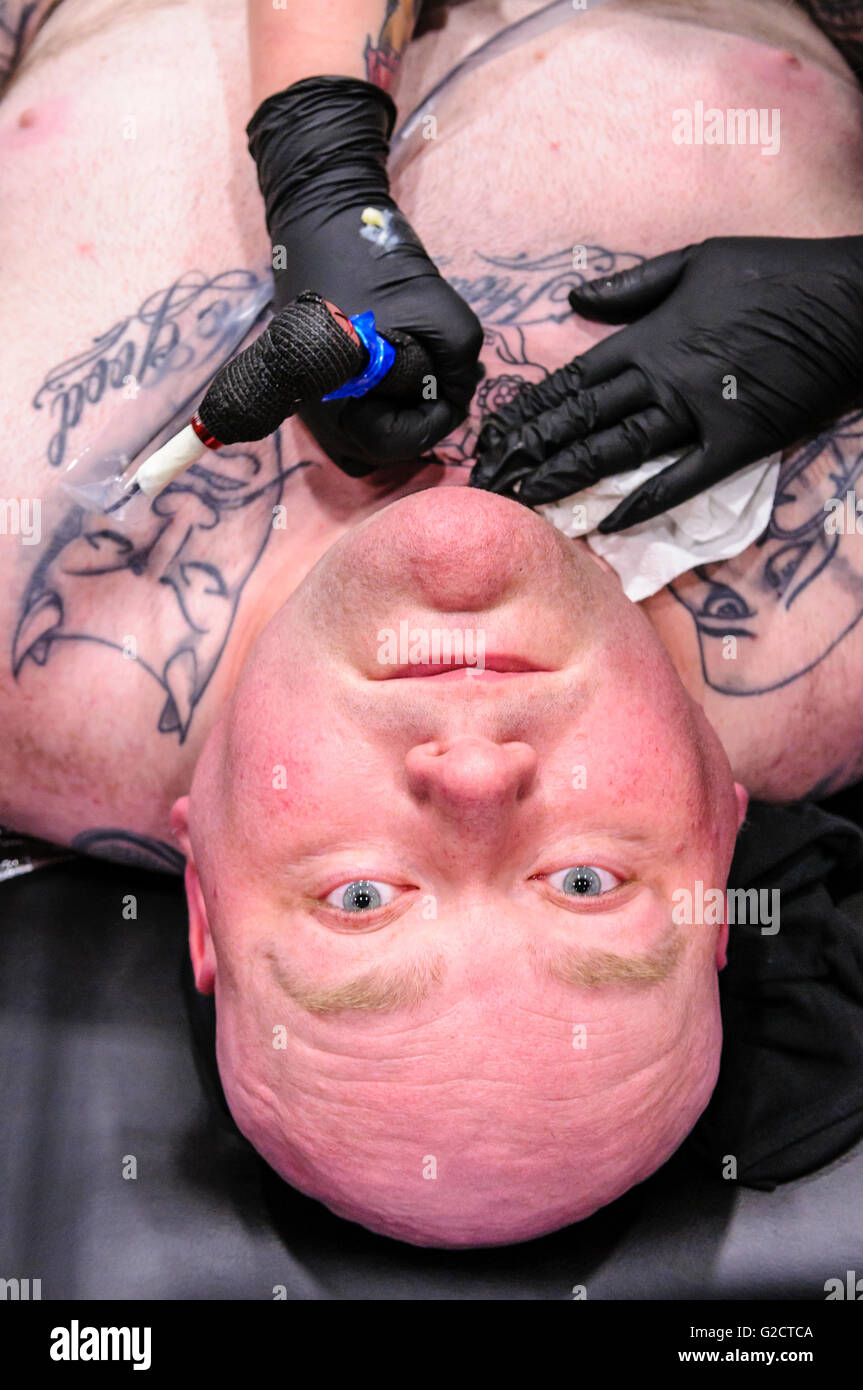 BELFAST, NORTHERN IRELAND. 28 MAY 2016 - 6th Northern Ireland Tattoo Conference. A male customer looks up as he has a tattoo on his throat and chest. Stock Photo