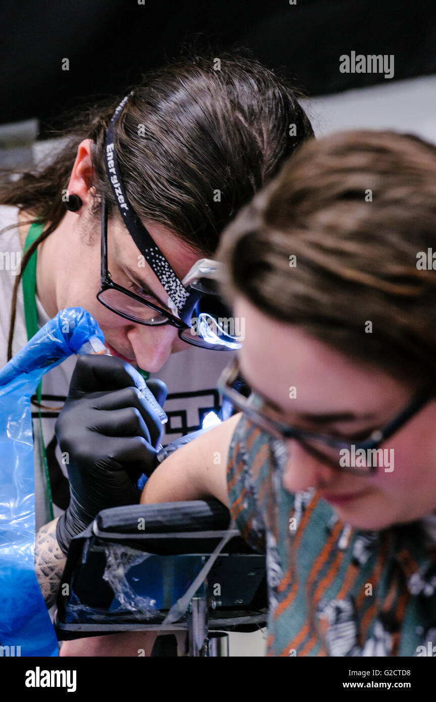 BELFAST, NORTHERN IRELAND. 28 MAY 2016 - 6th Northern Ireland Tattoo Conference. A tattoo artist draws an intricate tattoo on the arm of a female customer with the aid of a head torch Stock Photo