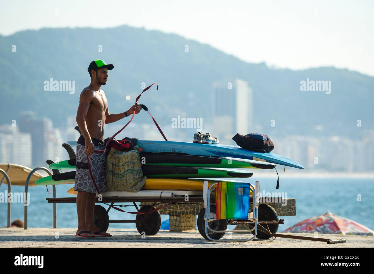 RIO DE JANEIRO - APRIL 5, 2016: Young carioca Brazilian man unpacks a stack of stand up paddle surfboards on Copacabana Beach. Stock Photo