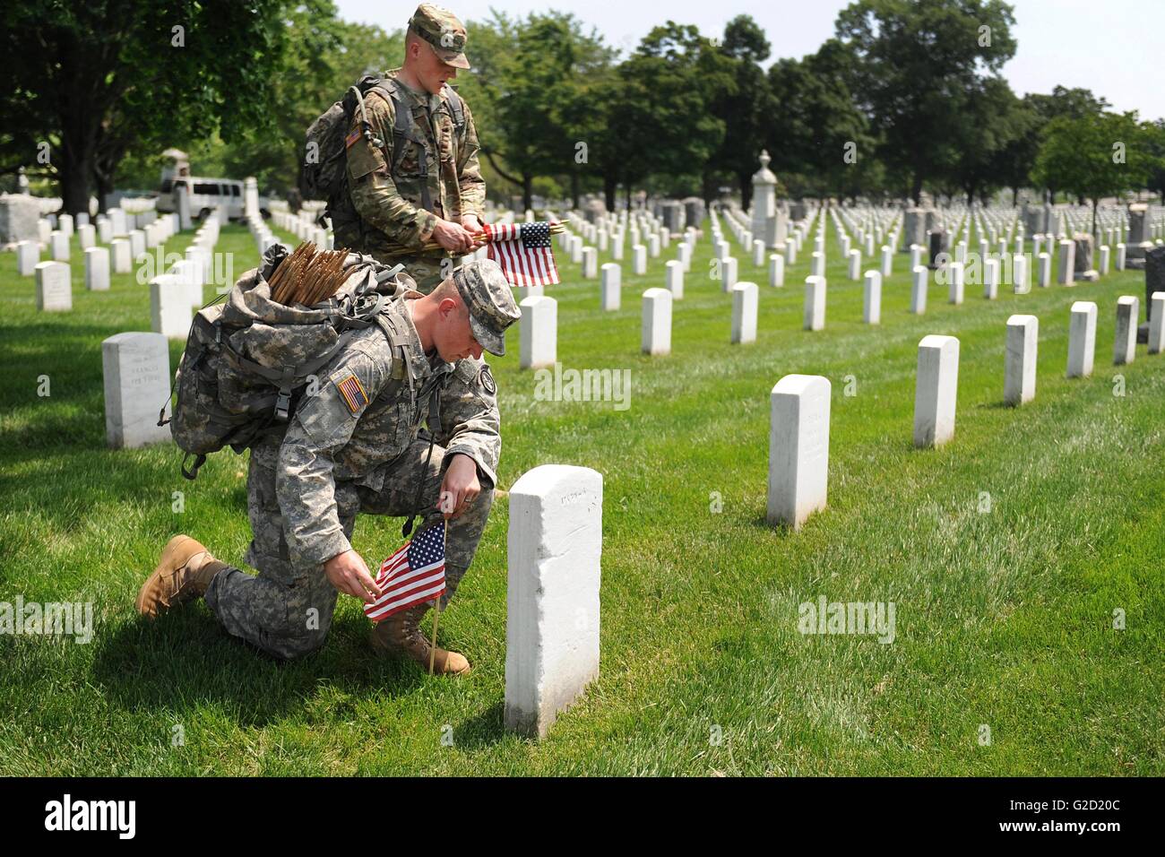 Arlington National Cemetery, Virginia, USA. 27th May, 2016. A U.S soldier with The Old Guard places an American flag in front of a grave stone in Arlington National Cemetery in honor of Memorial Day May 27, 2016 in Arlington, Virginia This tradition, known as 'Flags In,' has been conducted annually since The Old Guard was designated as the Army's official ceremonial unit in 1948. Credit:  Planetpix/Alamy Live News Stock Photo