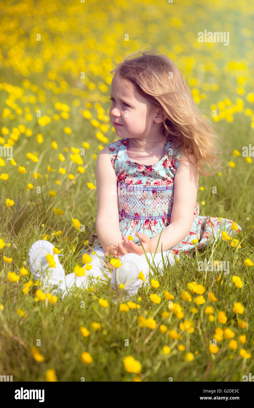 3 year old girl sitting in a meadow with yellow flowers Stock Photo