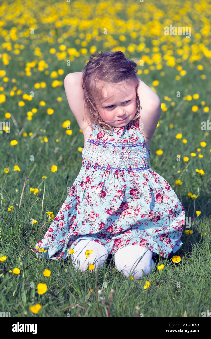 a 3 year old girl is sitting on a flower meadow Stock Photo