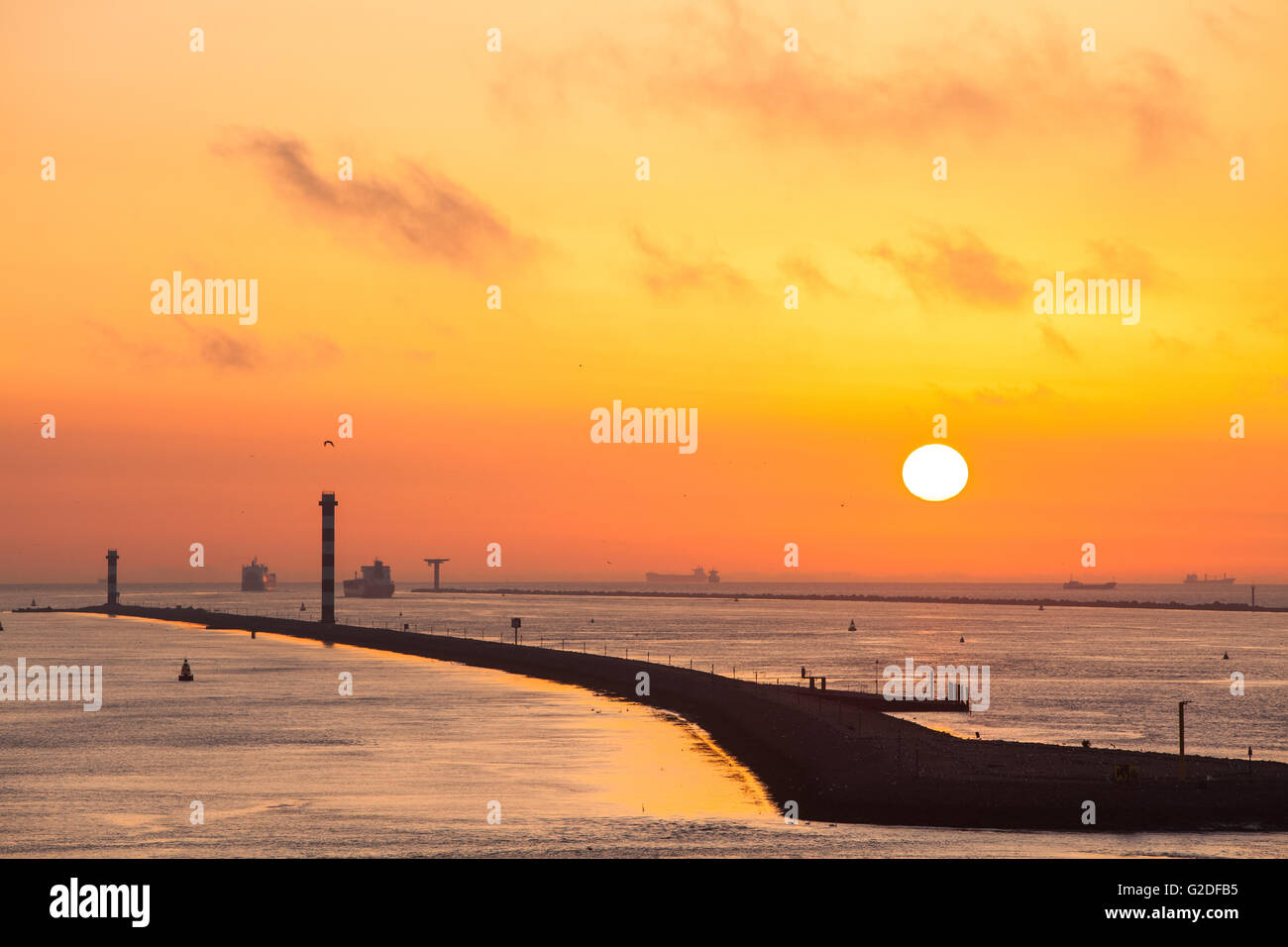 Jetty with ships in silhouette leaving Port of Rotterdam harbor Netherlands during sunset Stock Photo
