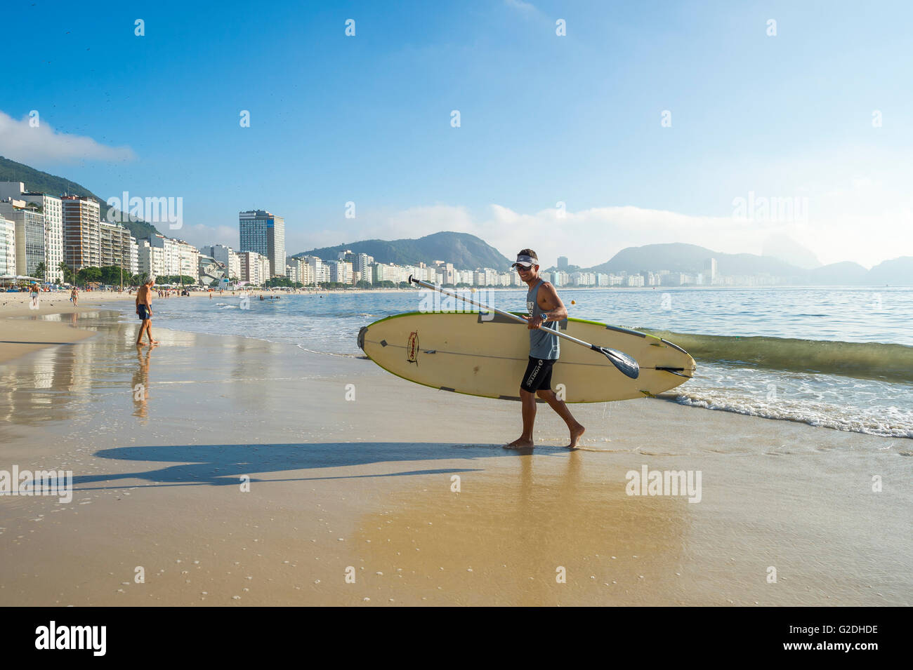 RIO DE JANEIRO - APRIL 5, 2016: A young Brazilian man carries a stand up paddle longboard surfboard on the Copacabana Beach. Stock Photo