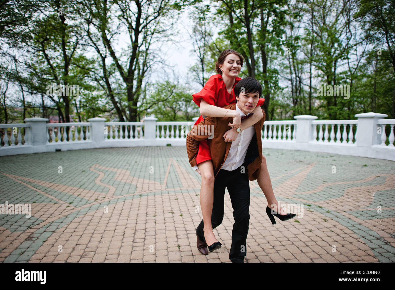 Happy couple walking in love. Stylish man at velvet jacket rolls his girl on his back. Stock Photo