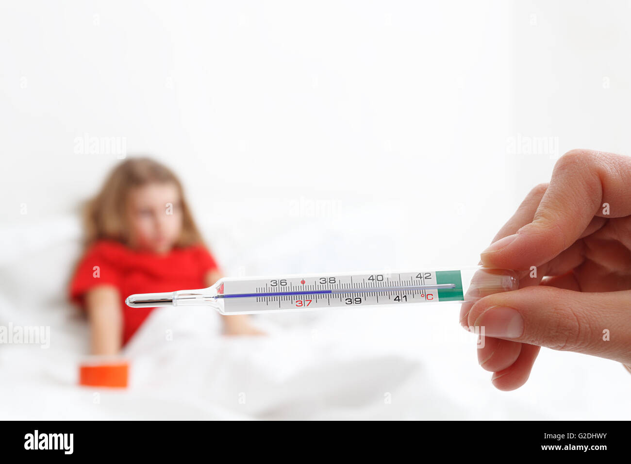 pediatric doctor hand holding a thermometer indicating fever with blurry child in background Stock Photo