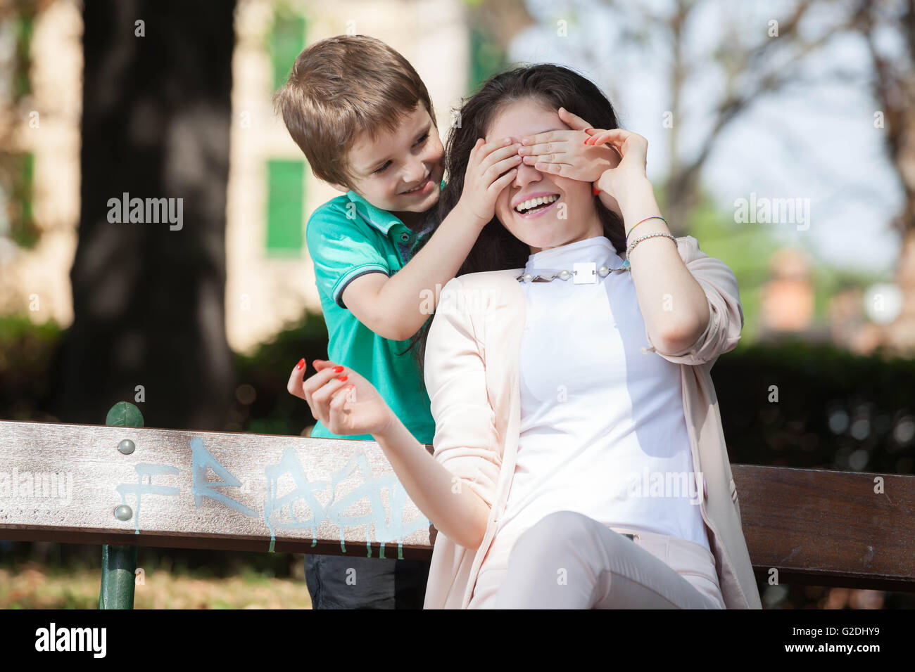 kid boy playing in the park guess who with his young mom or aunt Stock Photo