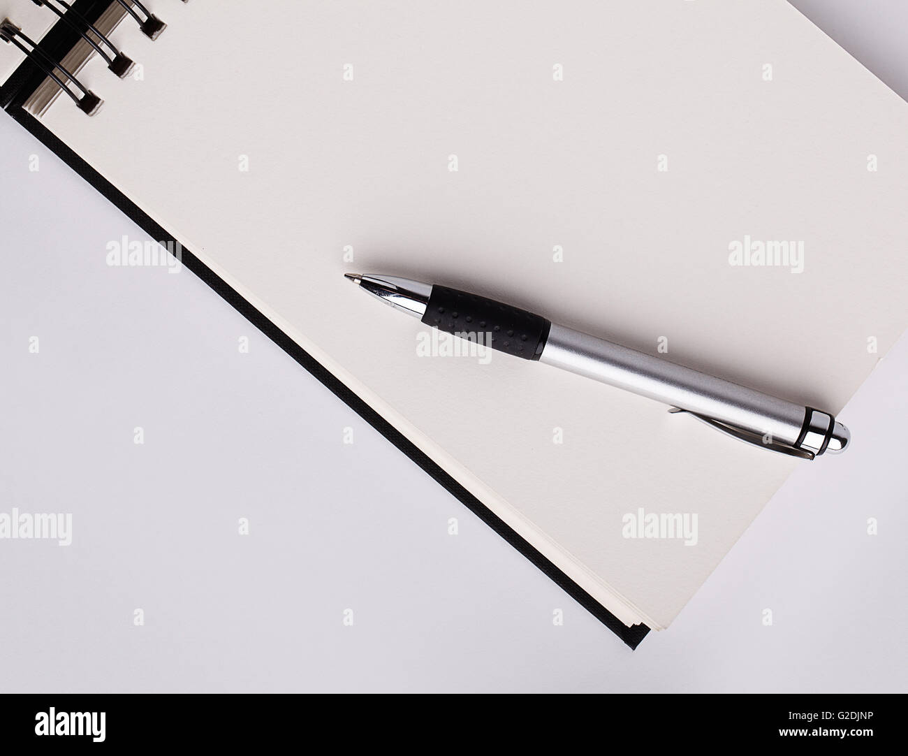 Metal ballpoint pen resting on an opened blank white notepad with copyspace for your message or text Stock Photo