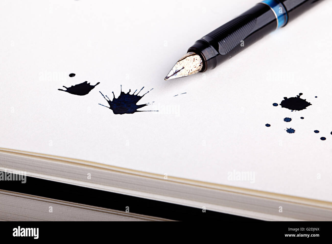 Three messy black ink splats with fountain pen opened to show the nib on white paper Stock Photo