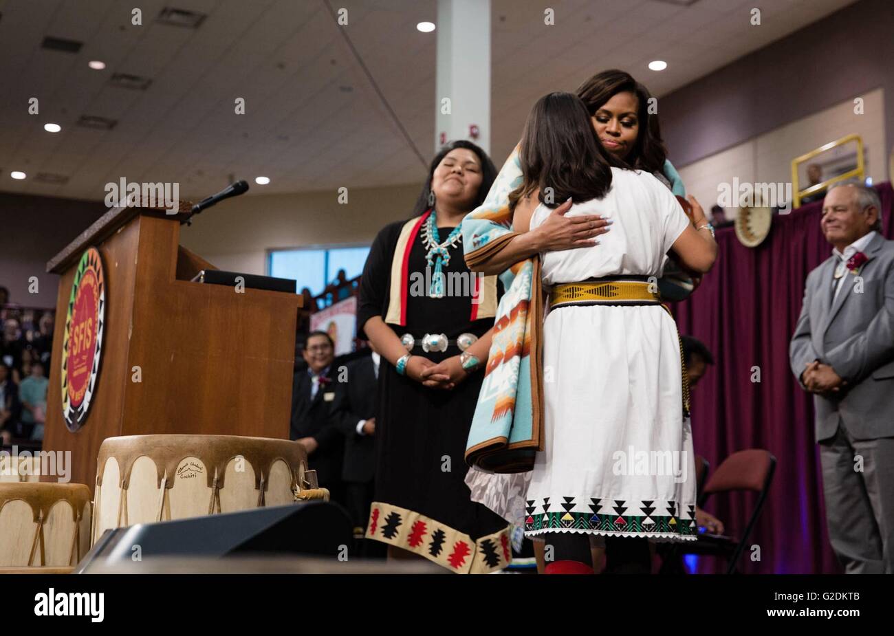 U.S First Lady Michelle Obama embraces Shilyn Platero-Fisher after she was presented with a traditional blanket during the Santa Fe Indian School high school commencement ceremony May 26, 2016 in Santa Fe, New Mexico. Stock Photo
