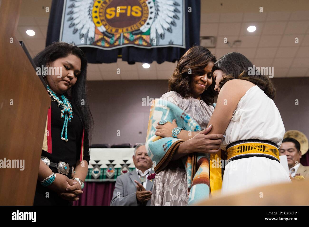U.S First Lady Michelle Obama embraces Shilyn Platero-Fisher after she was presented with a traditional blanket during the Santa Fe Indian School high school commencement ceremony May 26, 2016 in Santa Fe, New Mexico. Stock Photo
