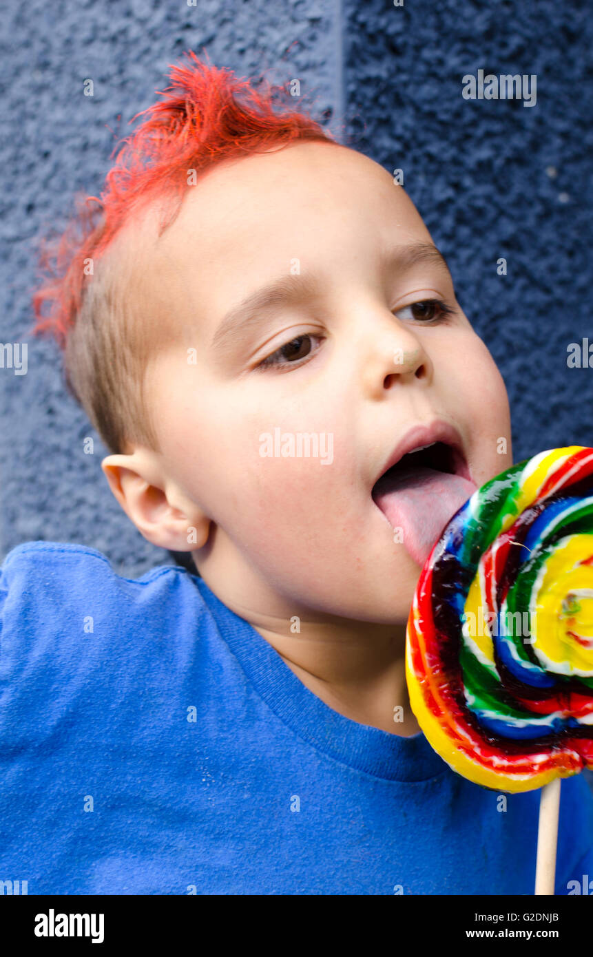 A young boy with an orange mohawk eats a large lollipop Stock Photo