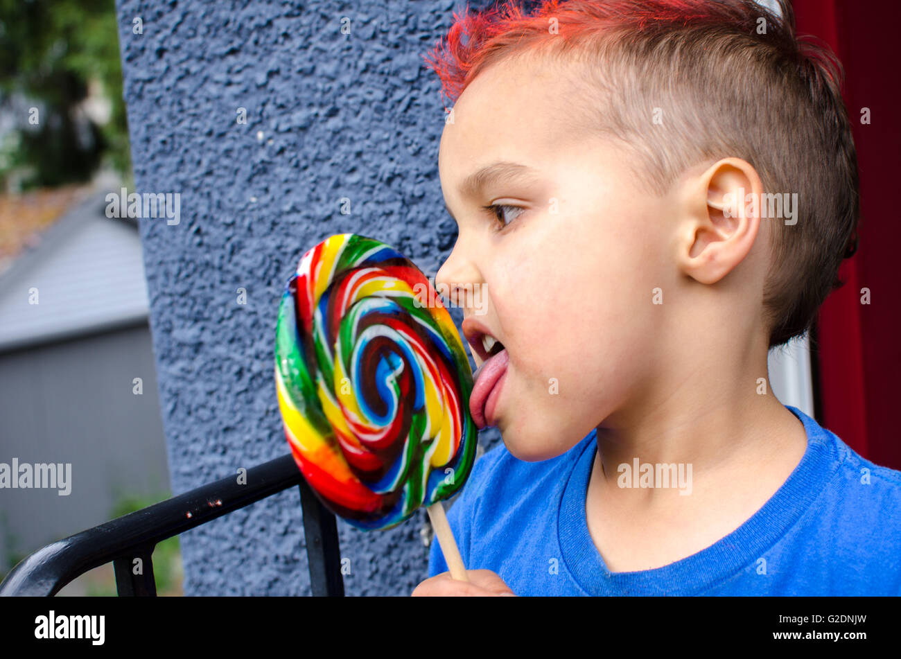 A young boy with an orange mohawk eats a large lollipop Stock Photo