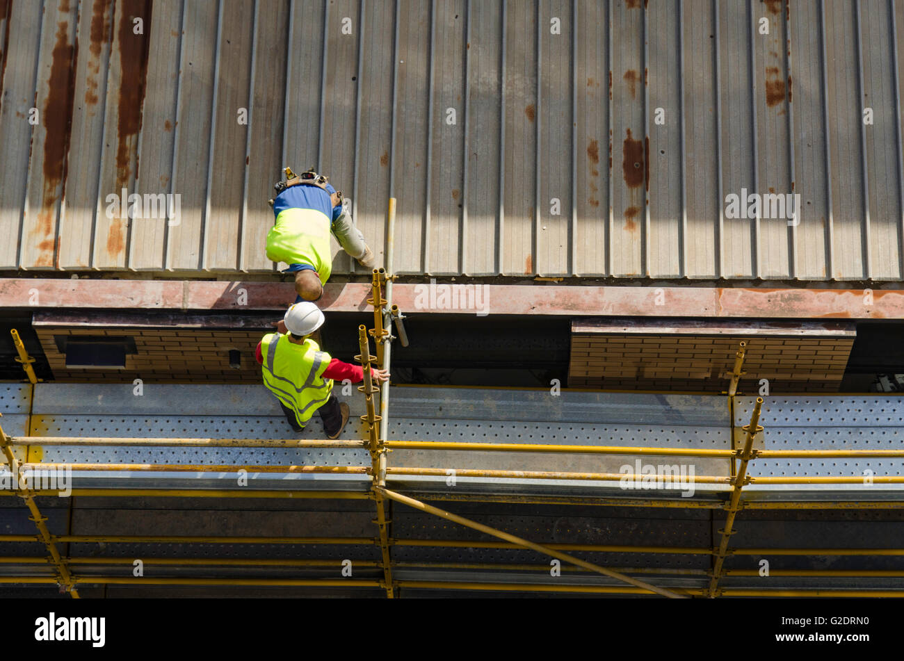 Looking down on men working in high visibility (hi-vis) apparel on the steel roof of a multistory building site, on yellow coloured scaffolding Stock Photo