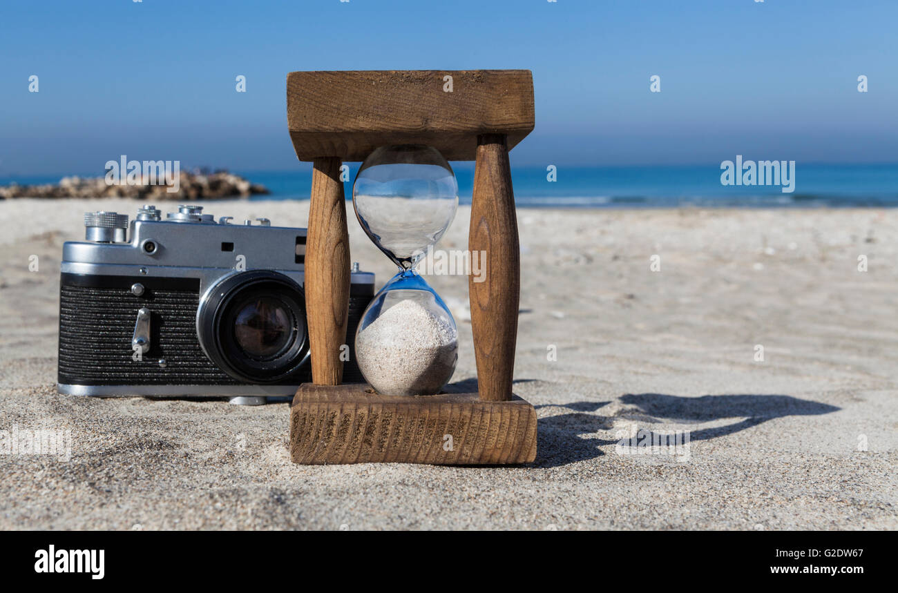 Old wooden hourglass and vintage camera on sand at sunny beach with ...