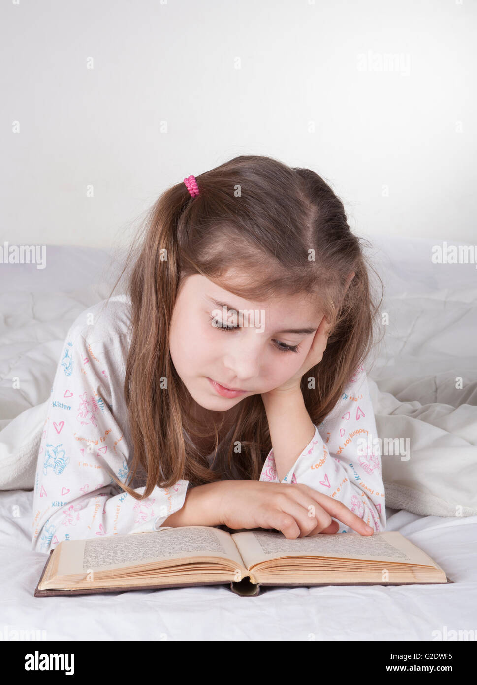 Little girl lying in bad and reading bible written in Hebrew Stock