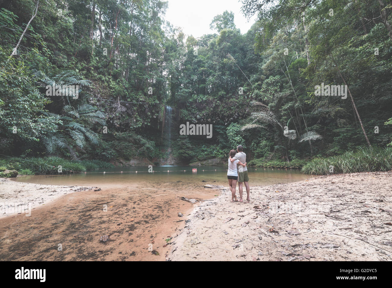 Couple of tourists looking at a stunning multicolored natural pool and waterfall in the rainforest of Lambir Hills National Park Stock Photo