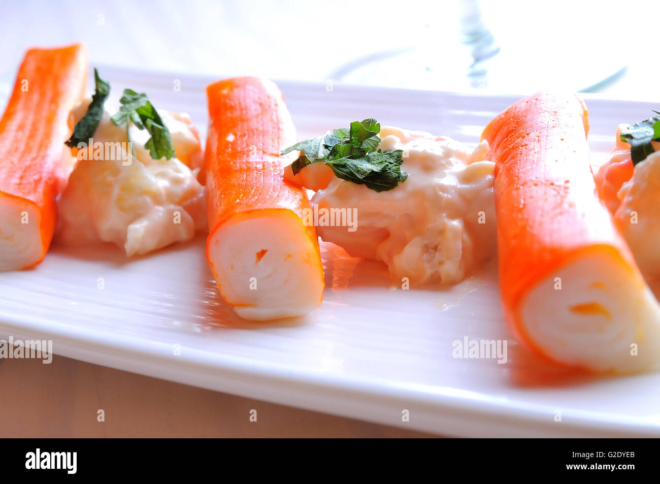 Surimi sticks with sauce on a white plate on a white wooden table front view Stock Photo