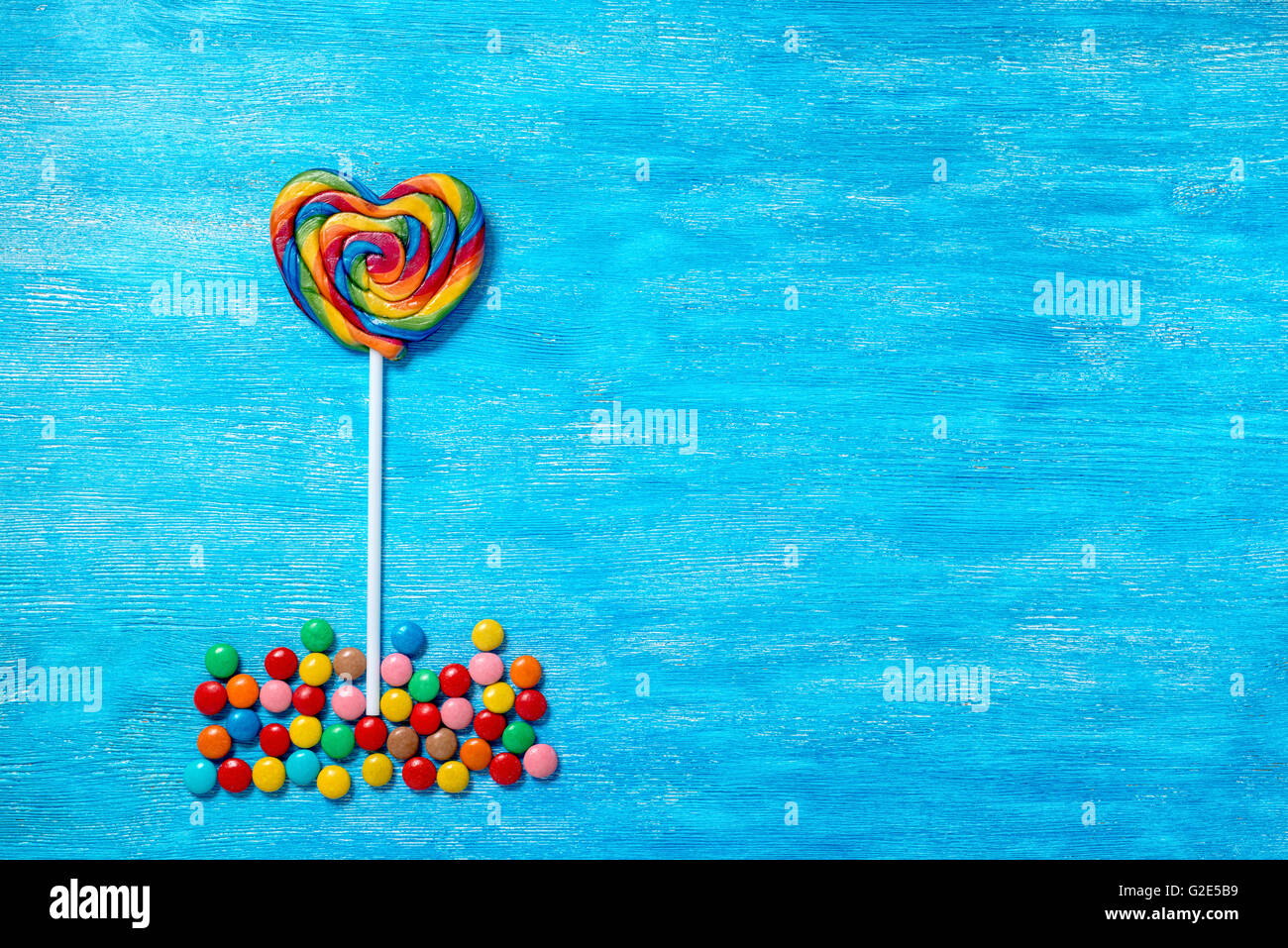 flat lay of beautiful multicolored lollipop shape heart and sweet bonbons on painted blue wooden background, close up Stock Photo
