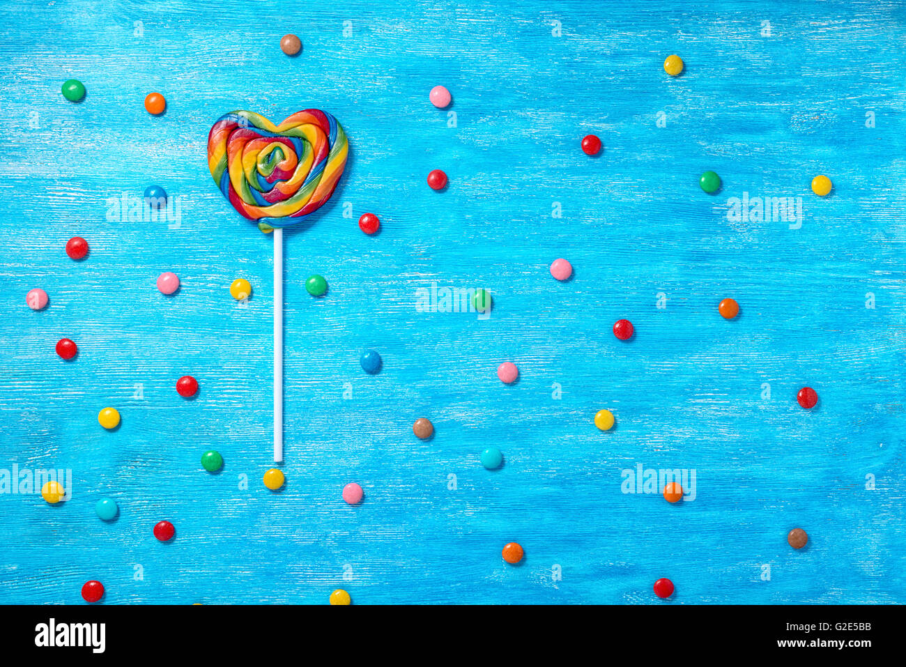 flat lay of beautiful colorful lollipop shape heart and scattered sweet bonbons on painted blue wooden background, close up Stock Photo