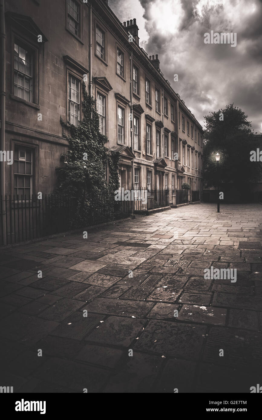 Row of Three-Story Townhouses and Illuminated Street Lamp Against Ominous Clouds Stock Photo