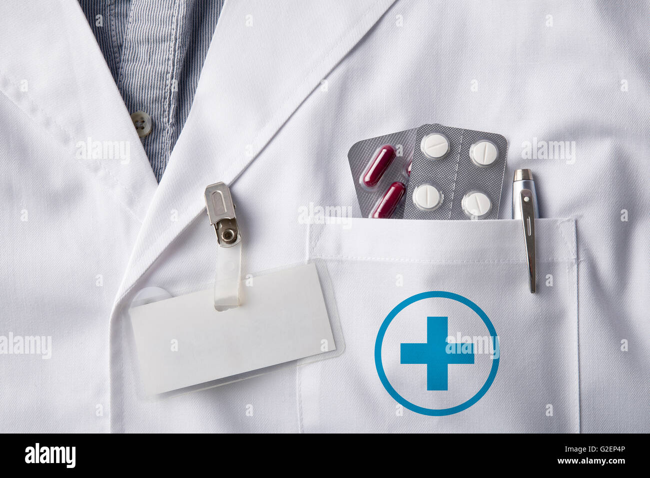 Close up white gown doctor with pills blisters and pen in pocket and identification tag blank. Horizontal composition. Front vie Stock Photo