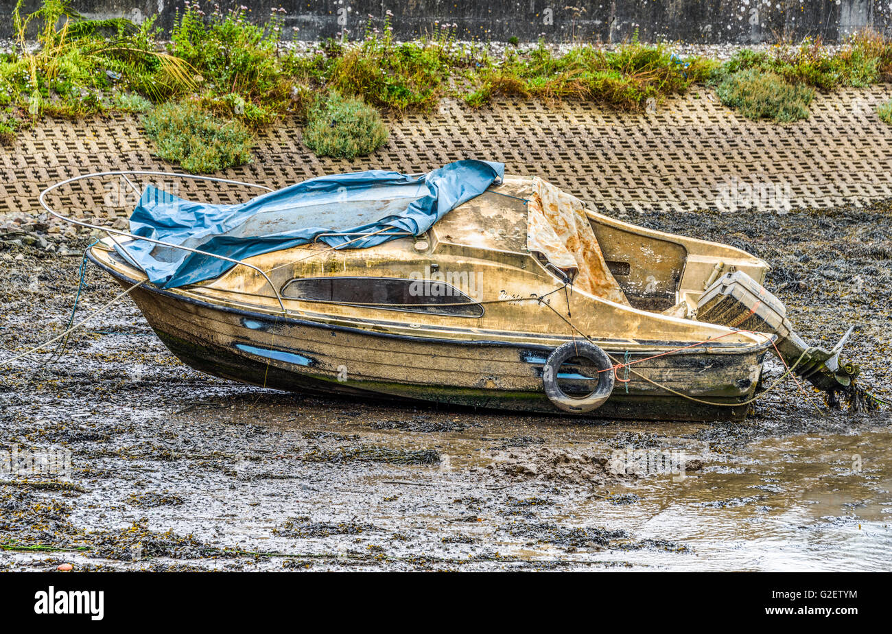 Seemingly abandoned small cabin cruiser lying on the mud at low tide and looking extremely worse for wear Stock Photo
