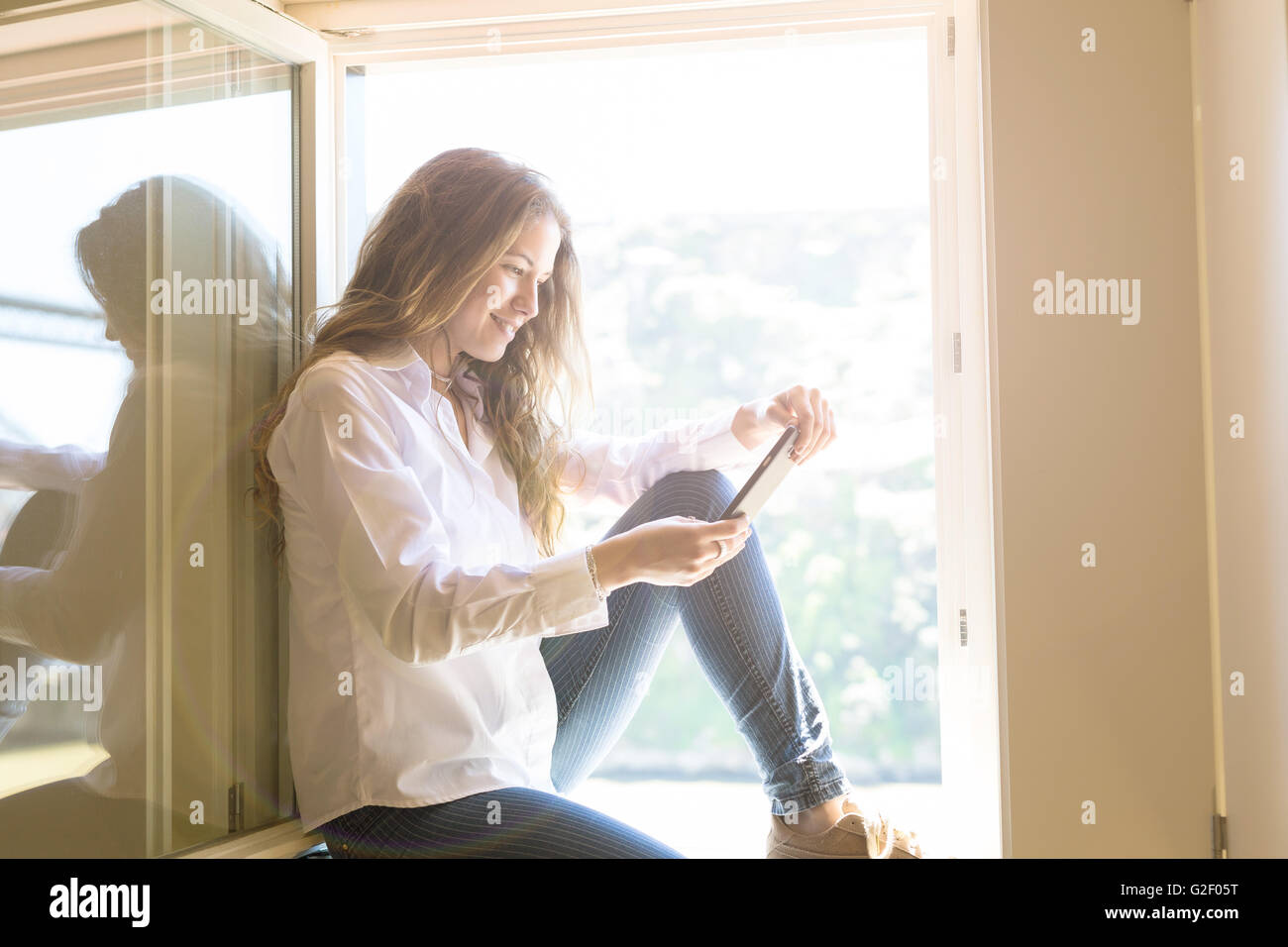 Young woman catching some sun at the balcony while using her new smartphone Stock Photo