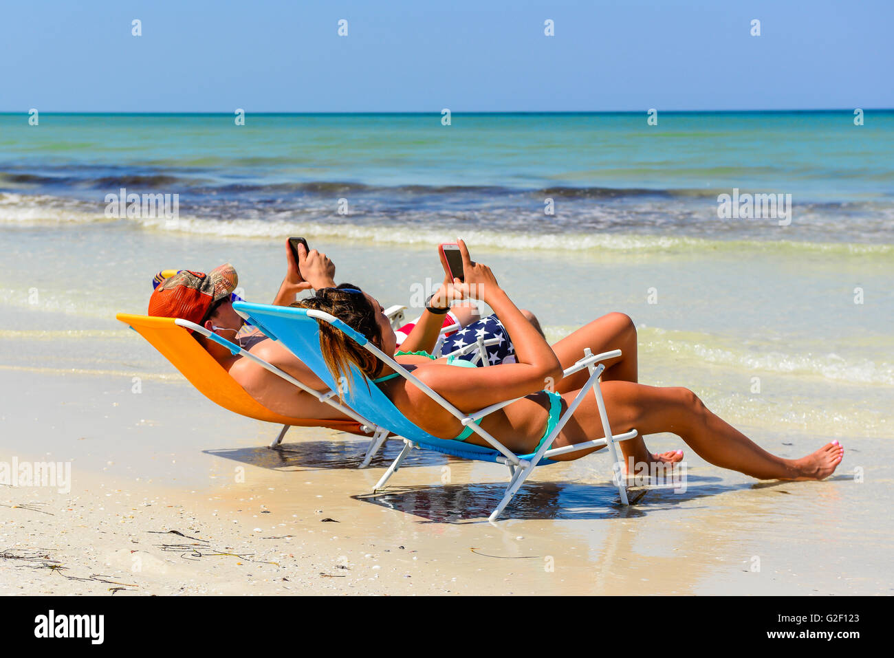Preoccupied couple can't stop looking at their cell phones while reclining in beach chairs the shoreline Stock Photo