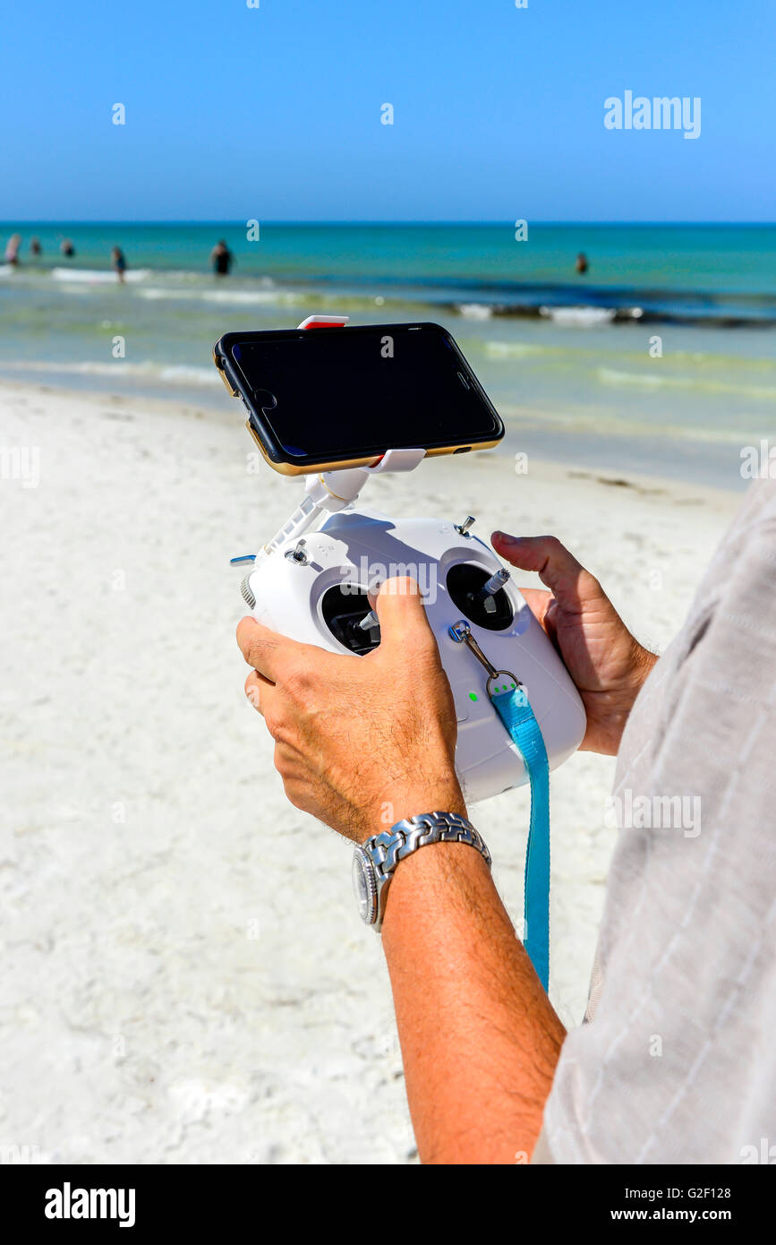 A man's hands holding a radio controller with joysticks piloting an unseen non-military drone flying overhead at the beach Stock Photo