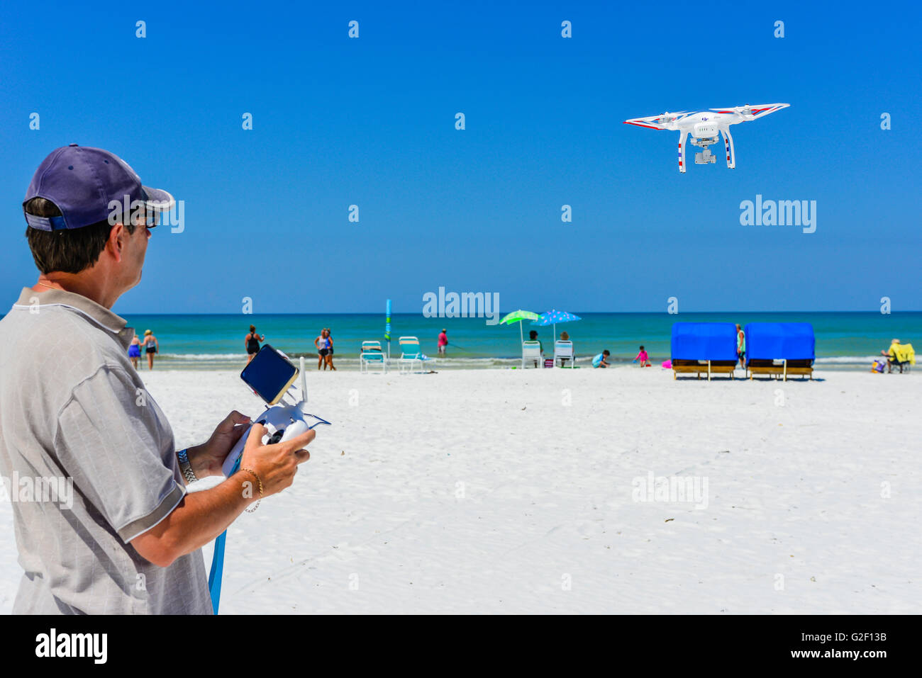 A drone pilot maneuvers the joy sticks on the radio controller for a flying non-military drone against blue skies at the beach Stock Photo