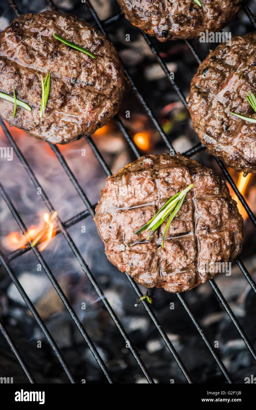 beef burgers on grill with flames from charcoal, overhead view Stock
