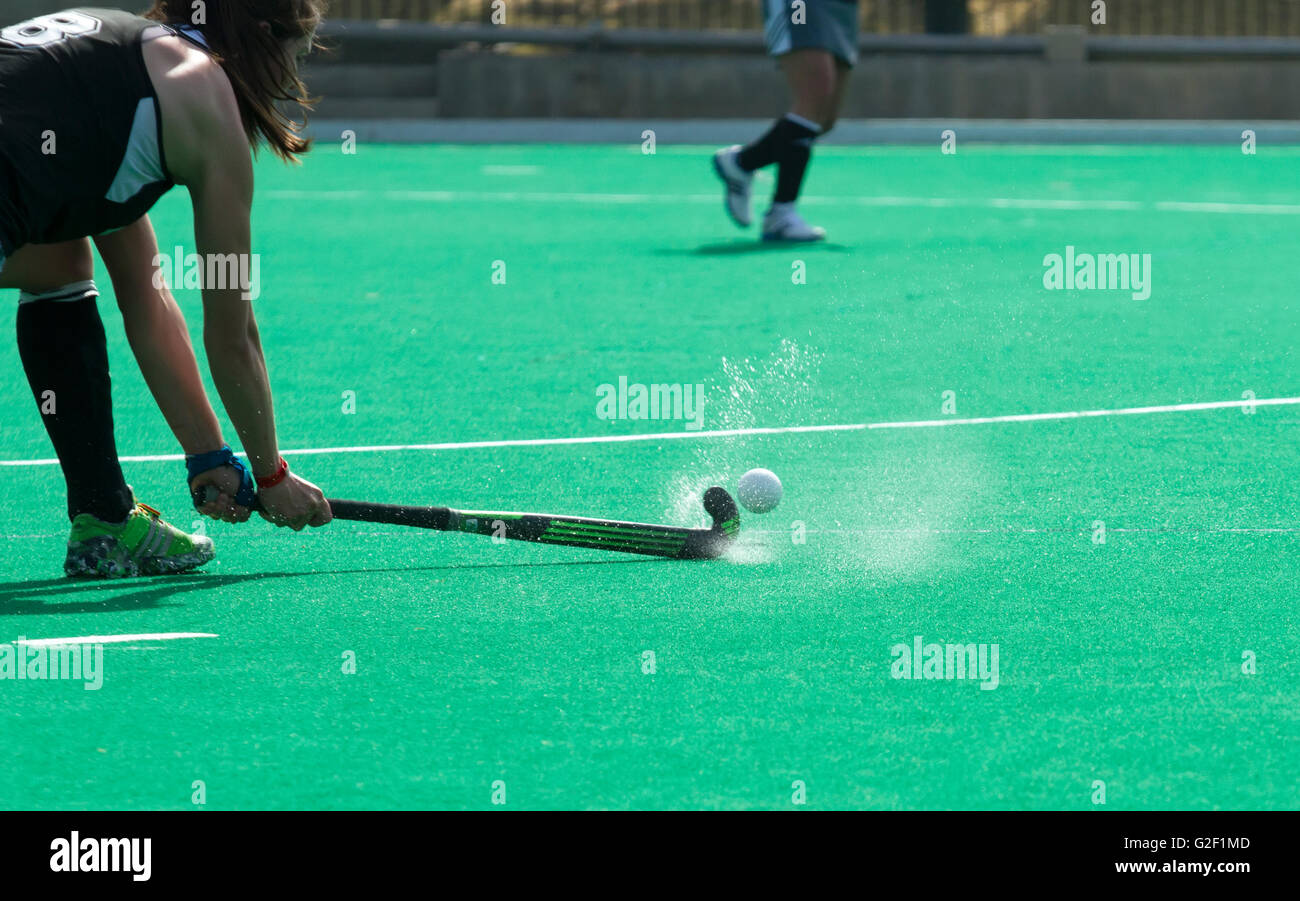 Field hockey player takes a shot as water splashes of the turf Stock