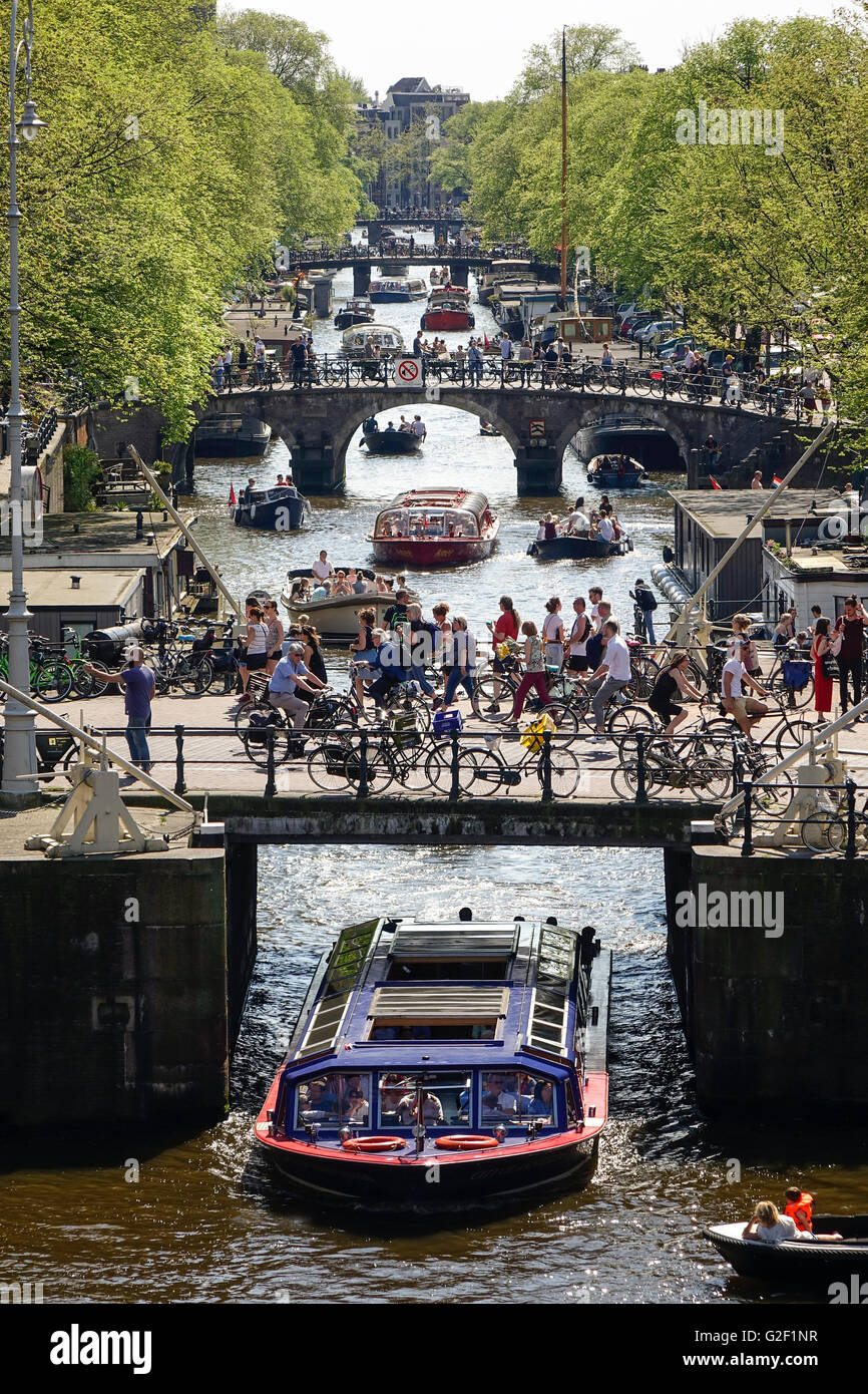 Amsterdam Canals. Four bridges with many cyclists on the Prinsengracht canal with canal tour boats and small pleasure boats in spring Stock Photo
