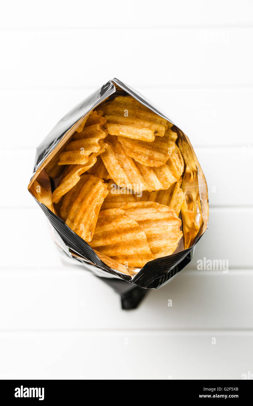 Crinkle cut potato chips on white table. Tasty spicy potato chips in