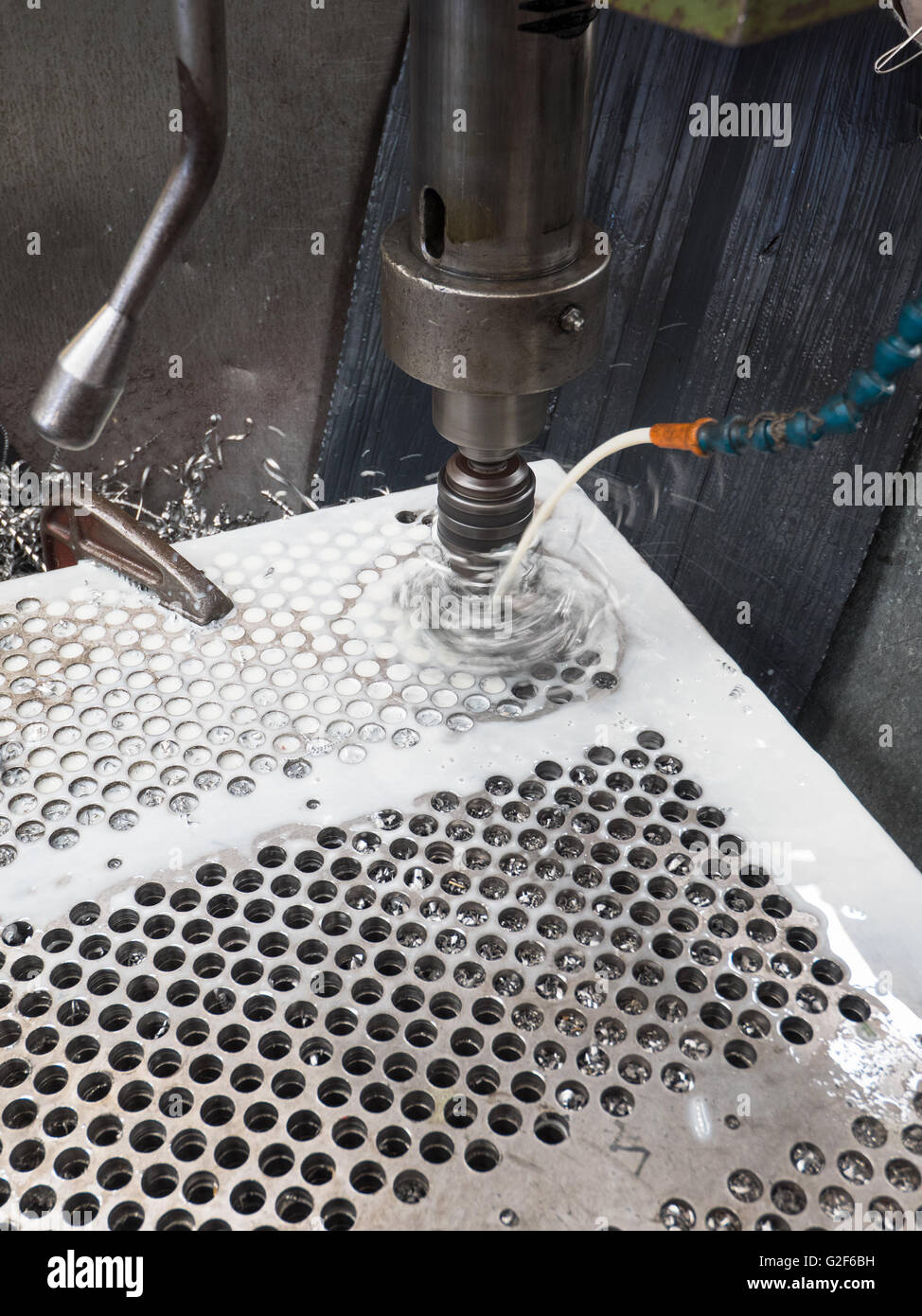 Column drilling machine making holes in a steel plate while being cooled down by cooling liquid. Stock Photo