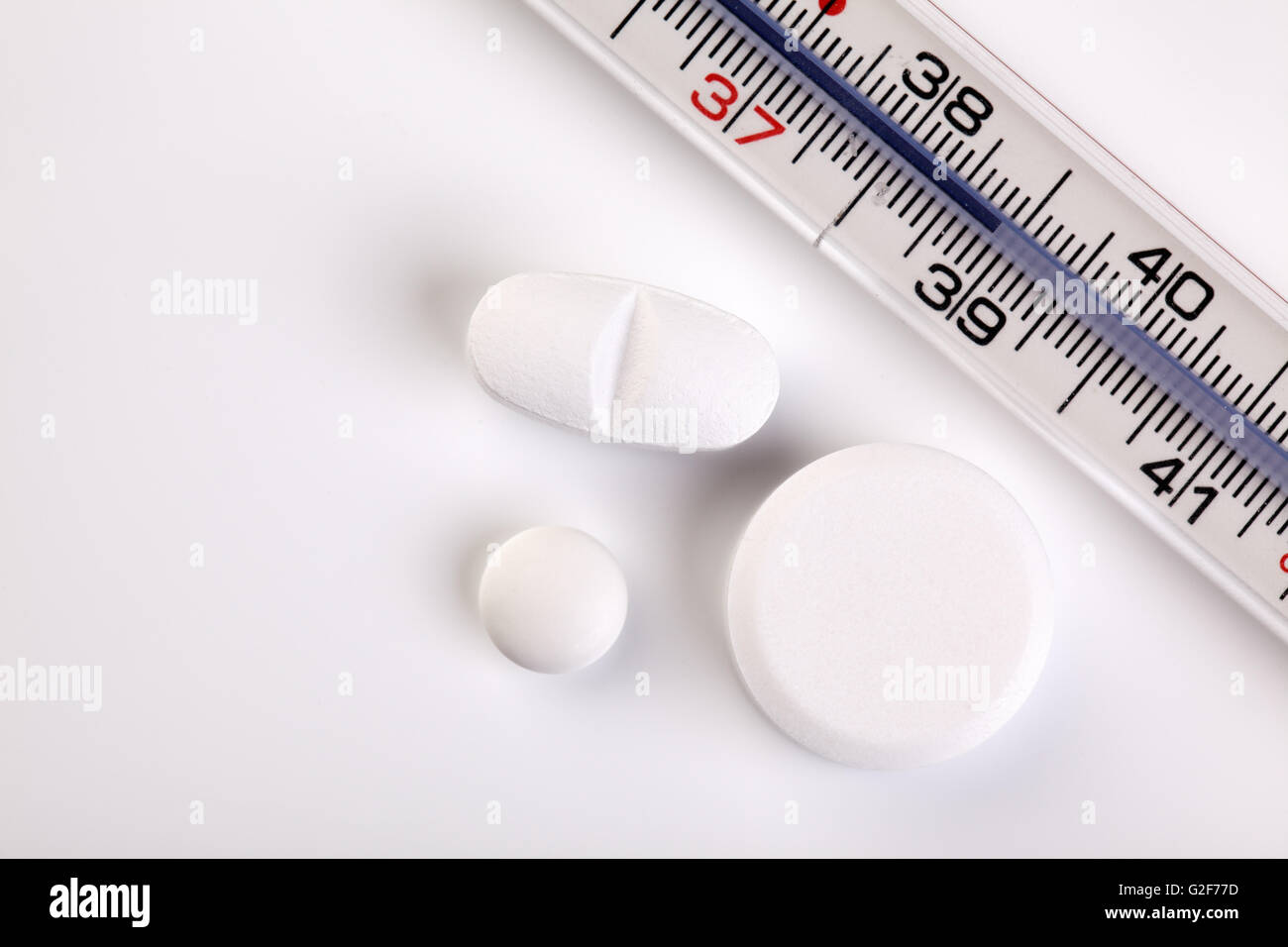 Fever thermometer showing a temperature of 39 degrees celsius and some pills Stock Photo