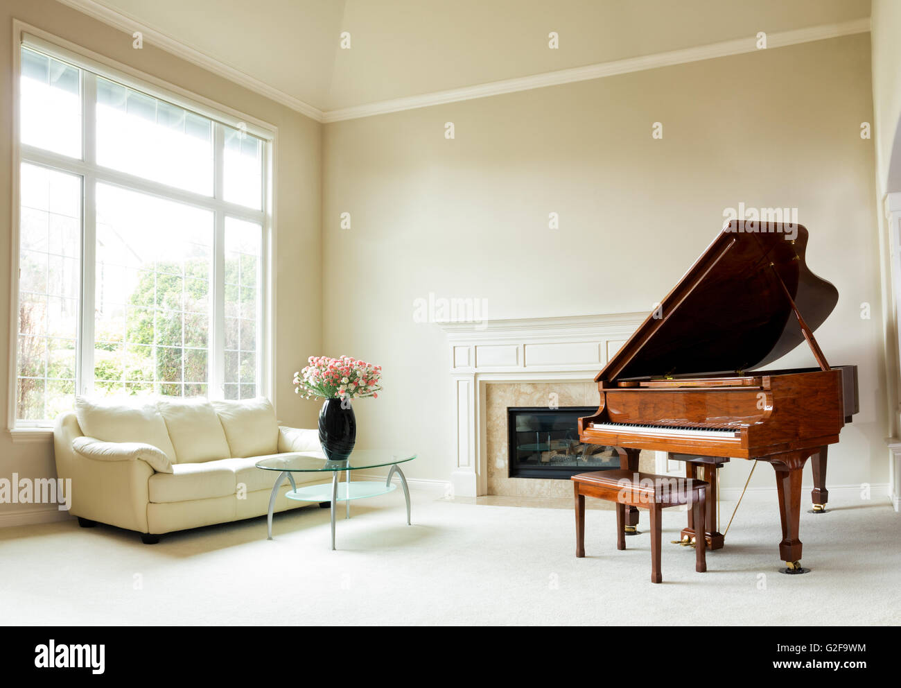 Living room with grand piano, fireplace, sofa and large window with bright daylight coming through. Stock Photo