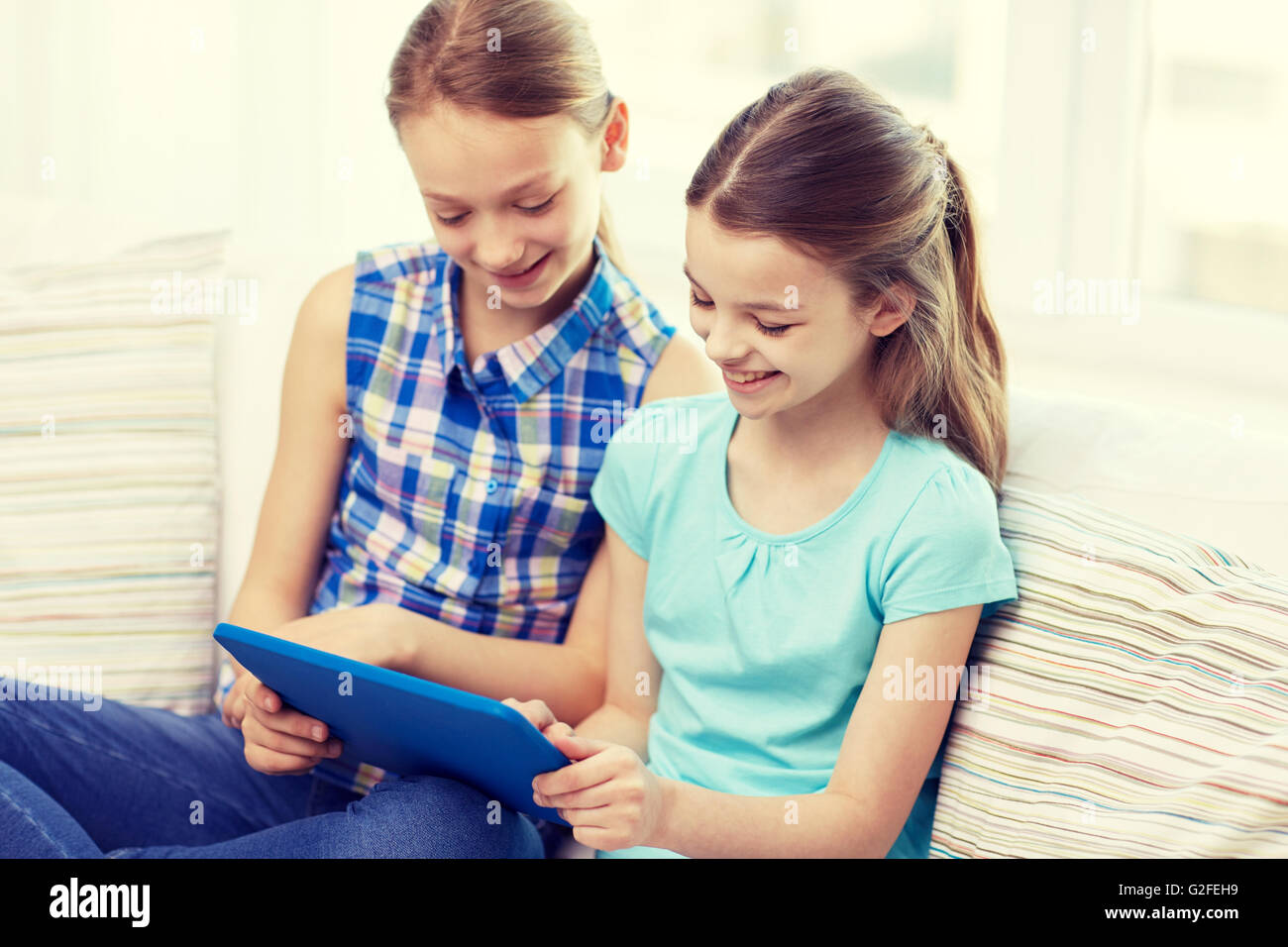 happy girls with tablet pc sitting on sofa at home Stock Photo - Alamy