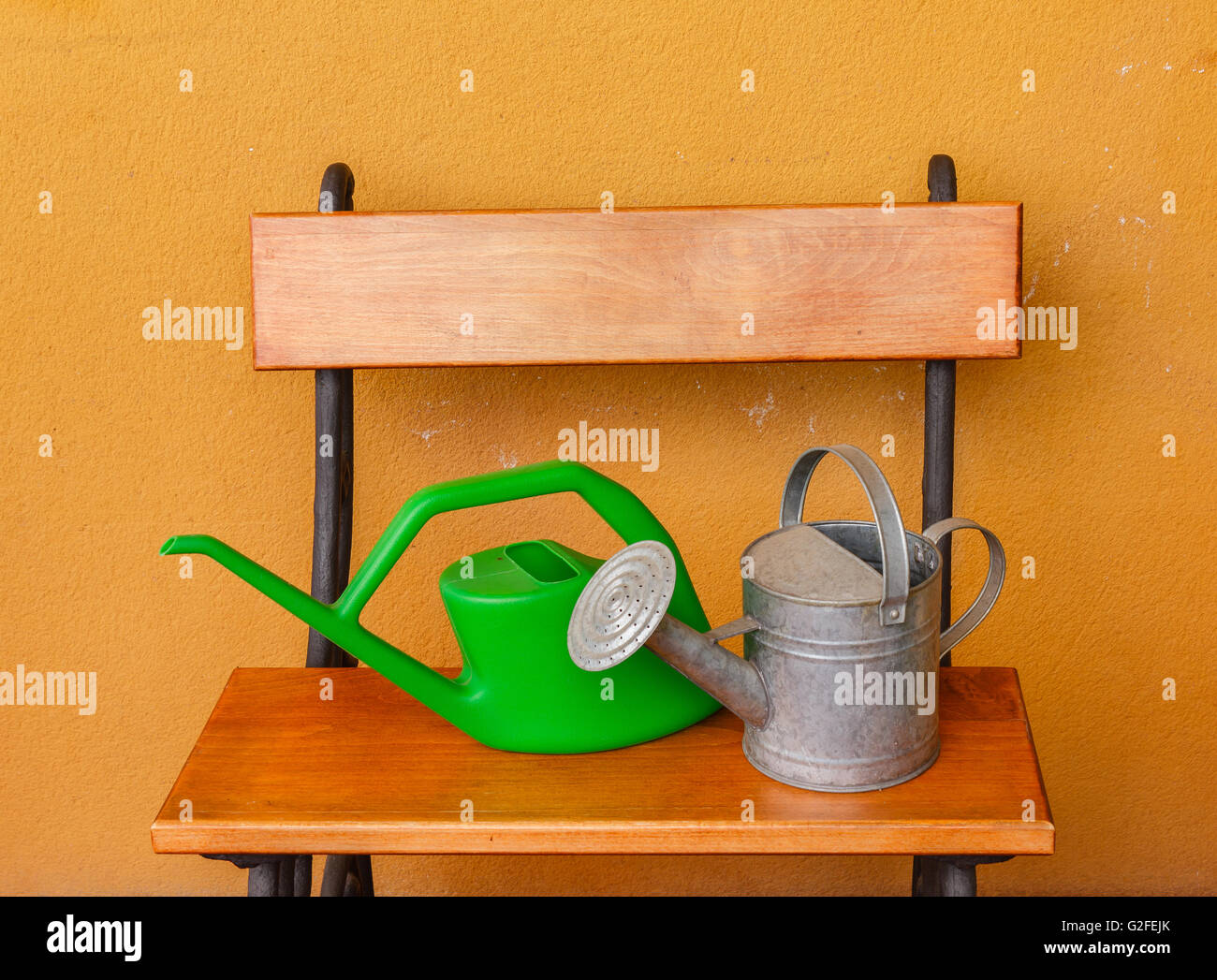 a corner of the terrace with  a wooden bench and a watering-can of aluminium  and a plastic one Stock Photo
