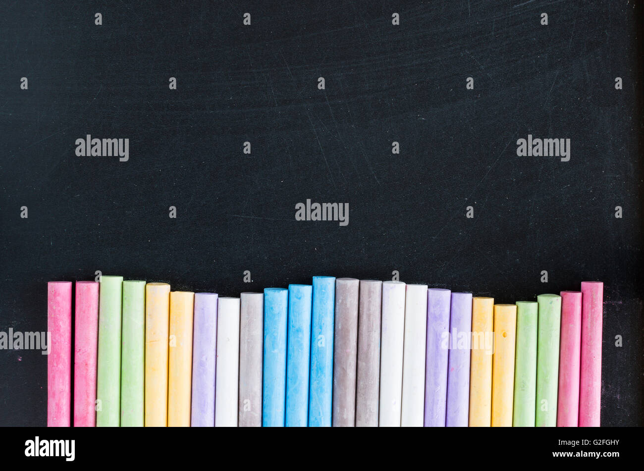 Colorful chalks lined up on school blackboard background Stock Photo