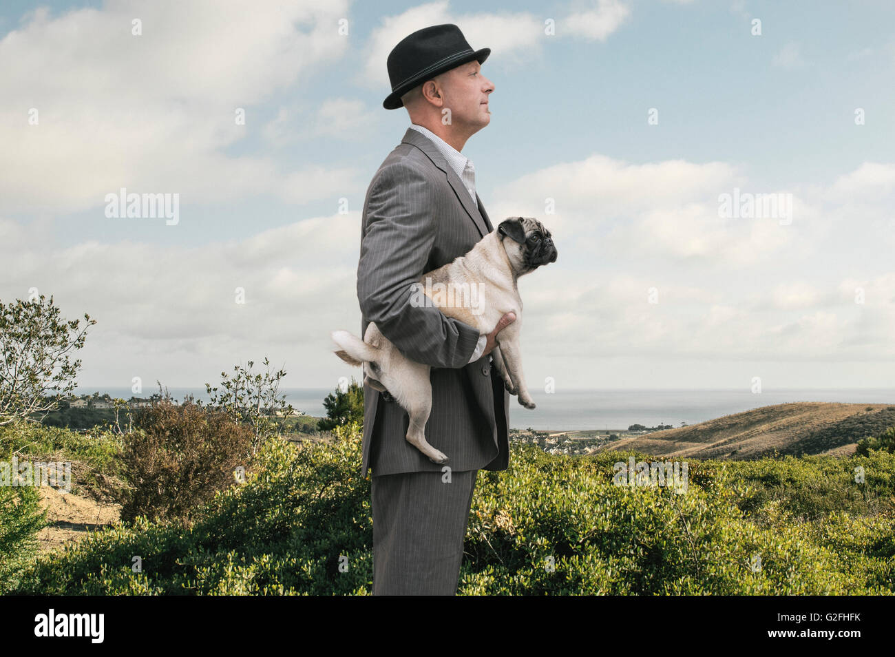 Profile of Businessman Holding Dog with Hills and Ocean in Background Stock Photo