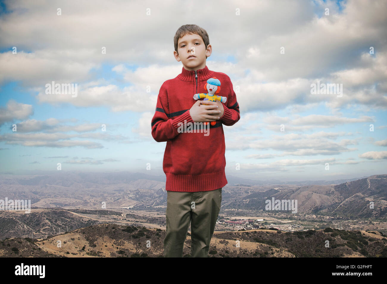 Young Boy Holding Stuffed Doll Against Mountain Landscape Stock Photo