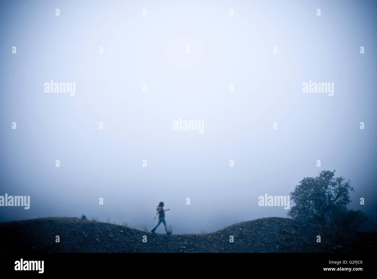 Woman Walking Over Hills in Fog Stock Photo