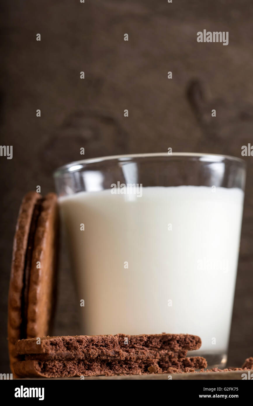 Bitten biscuit and one glass of milk in background on old wooden table Stock Photo