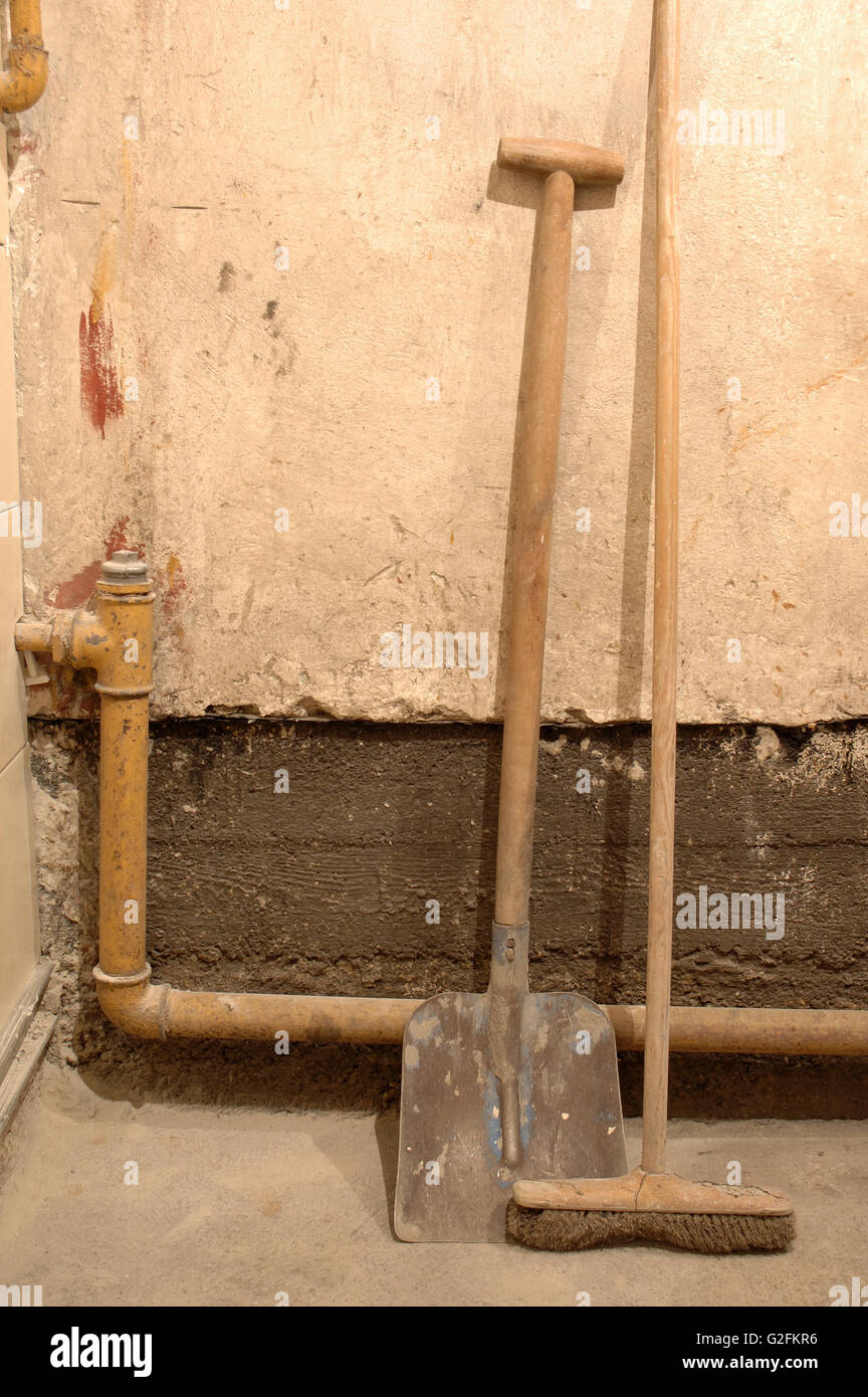 Old shovel and besom standing at dirty wall Stock Photo
