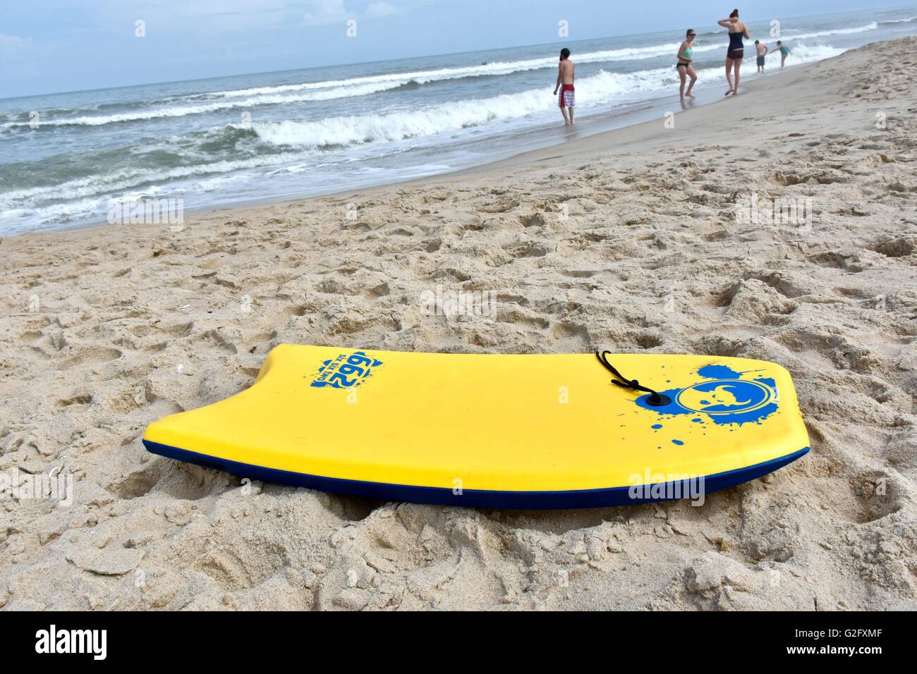 A yellow boogie board laying in the sand on the beach Stock Photo
