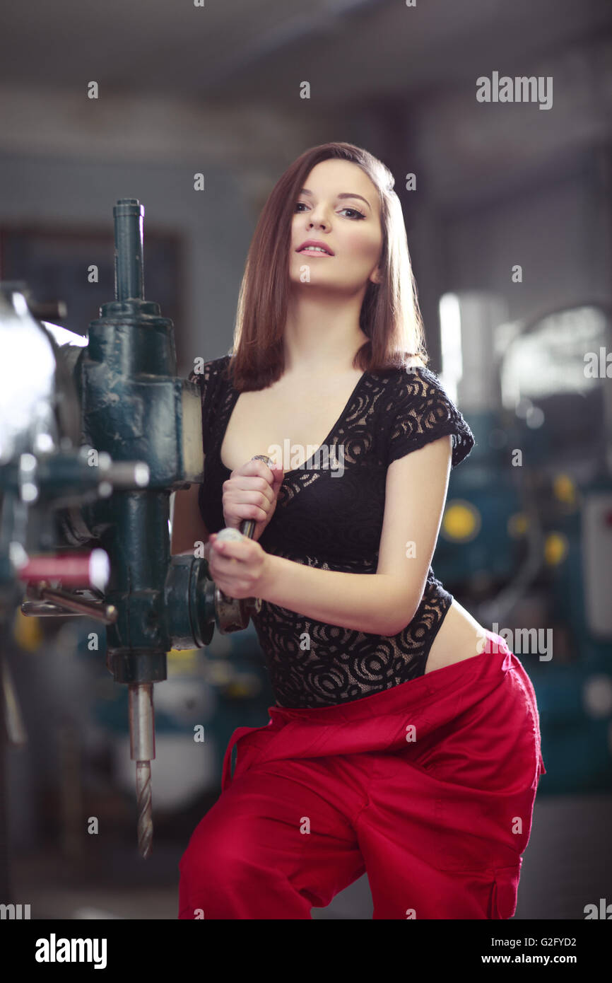 Sexy woman in red wear uniform working by drill machine on the factory. Stock Photo