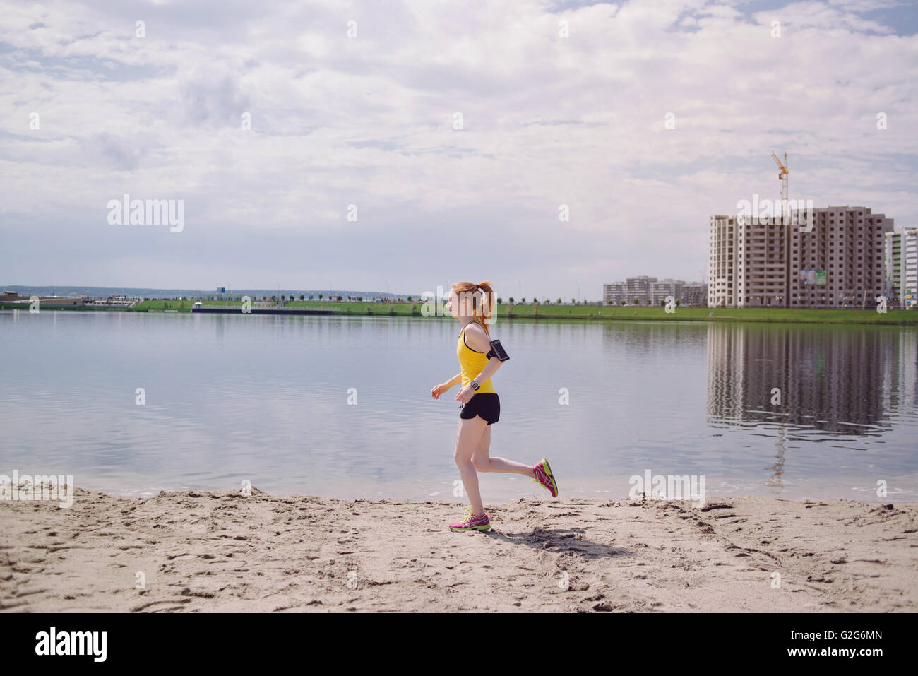 Young healthy lifestyle woman running at sunrise beach. Girl running at sand near water on city's beach. Girl running in yellow Stock Photo