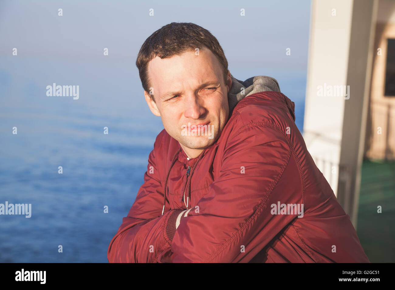 Young handsome Caucasian man standing on the walking deck of cruise ship in bright evening sunlight Stock Photo